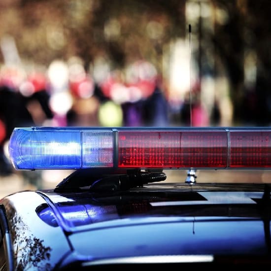 A police car with its lights on and the sun shining.